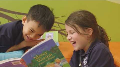Two young students laughing together over a picture book.