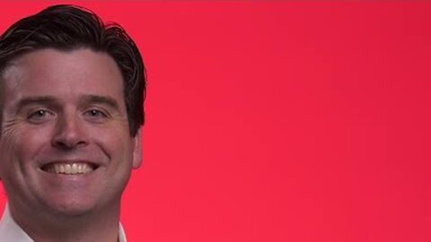 Patrick, smiling, in front of a red background.