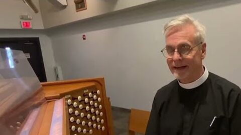Fr. Larry, smiling, seated at the organ console.