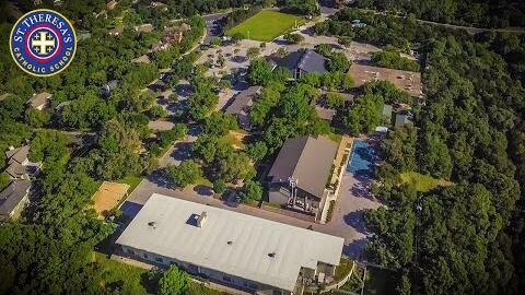 Aerial view of the campus: school and church roofs among thick green trees, with a playing field beyond.