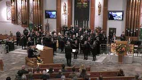 A large choir at the front of the church, with organ pipes on either side, the organ console at left, and people in the pews.