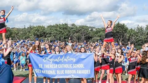 Cheerleaders and a crowd of students on the field behind a banner: Congratulations, St. Theresa Catholic School, 2023 National Blue Ribbon Awardee.