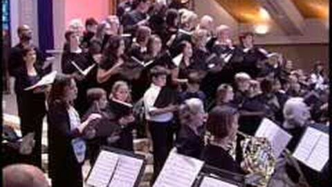 A large choir in black, with orchestra players and their music stands in front.
