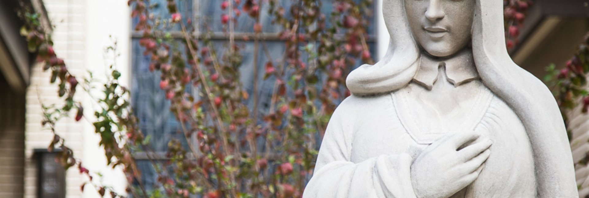 Statue of St. Theresa on campus with a stained glass window behind